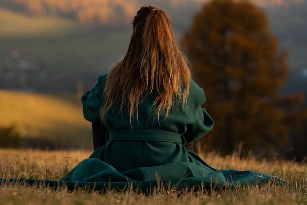 Femme assise dans l'herbe, manteau vert, regard vers l'horizon