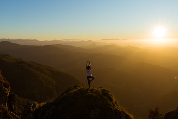 Femme en posture de yoga au sommet d'une montagne au lever du soleil